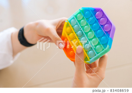Close-up top view of of unrecognizable young woman playing with rainbow pop-it fidget toy sitting at table. Close-up top view of of unrecognizable young woman playing with rainbow pop-it fidget toy sitting at table. 83408659