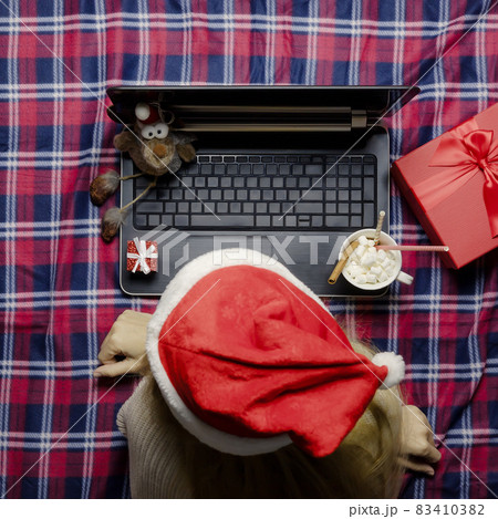 Lady santa at a laptop in a cozy Christmas home atmosphere. Writing holiday greetings. Waiting for Christmas. Lady santa at a laptop in a cozy Christmas home atmosphere. Writing holiday greetings. Waiting for Christmas. 83410382