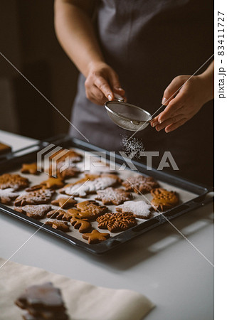 Baker sprinkles icing sugar from a sieve on Christmas gingerbread, Baker sprinkles icing sugar from a sieve on Christmas gingerbread, 83411727