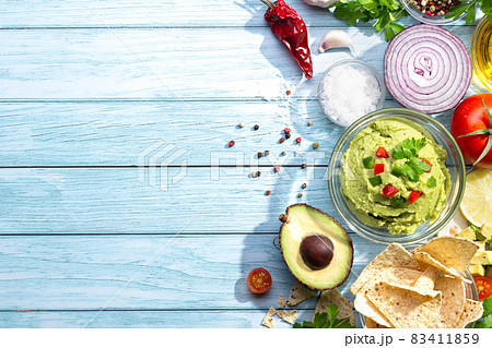 Bowl of guacamole and nachos with ingredients on blue background. with copy space. Top view. 83411859