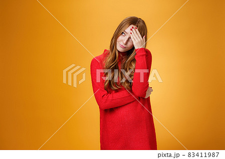 Annoyed and pissed embarrassed woman hiding behind hand making facepalm gesture looking away with irritated humiliated gesture, standing fed up and intense against orange background 83411987