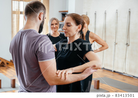 Yoga Trainer helping woman to stand on sadhu yoga board during yoga class, barefoot on a bed of nails 83413501
