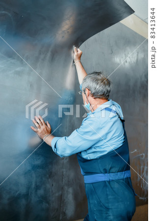 An elderly worker sheathes the walls with metal sheets. Real scene of work.Construction and repair. An elderly worker sheathes the walls with metal sheets. Real scene of work.Construction and repair. 83413644