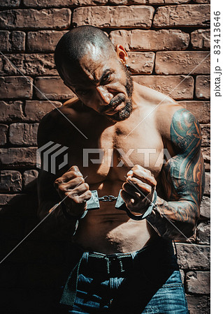 A bandit or rapist in tattoos is imprisoned in solitary confinement. Hands in handcuffs. A dangerous A bandit or rapist in tattoos is imprisoned in solitary confinement. Hands in handcuffs. A dangerous 83413646