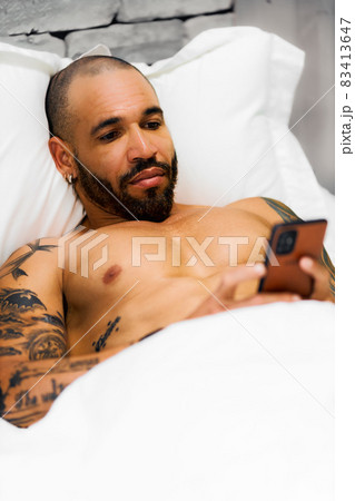 A bearded man lies in the post and corresponds on the phone. A sexy Cuban with a naked torso looks A bearded man lies in the post and corresponds on the phone. A sexy Cuban with a naked torso looks 83413647