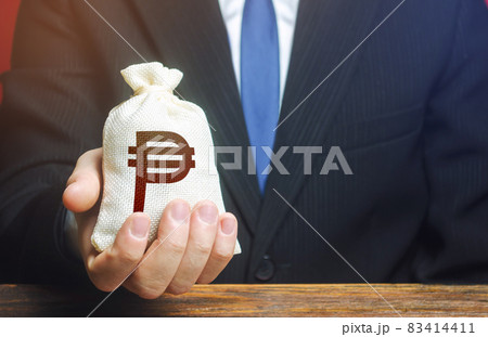 A businessman holds in his hand a philippine peso money bag. nvestments, financing. Stimulating economic recovery. Providing business with preferential loans and support during the economic crisis. I A businessman holds in his hand a philippine peso money bag. nvestments, financing. Stimulating economic recovery. Providing business with preferential loans and support during the economic crisis. I 83414411