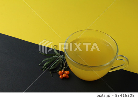 sea buckthorn tea drink on a black yellow bright background. Sea buckthorn drink tea juice in a glass cup next to a spout of sea buckthorn leaves orange berries on a black and yellow background. sea buckthorn tea drink on a black yellow bright background. Sea buckthorn drink tea juice in a glass cup next to a spout of sea buckthorn leaves orange berries on a black and yellow background. 83416308