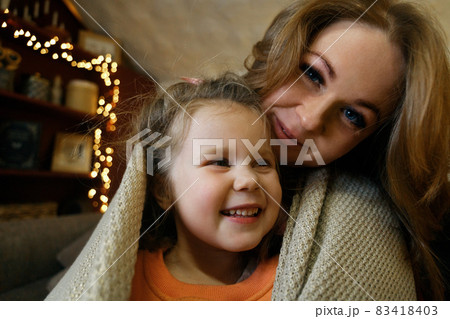 Close-up portrait of blond funny little girl with her mother in festive interior with garlands 83418403