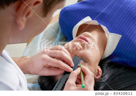 plastic surgeon and young woman with correction lines before cosmetic surgery, drawing lines on eyes 83420611