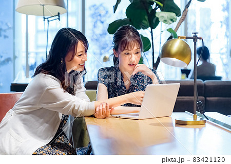 カフェでパソコンを見ながらミーティングする私服のビジネスウーマン2人  83421120