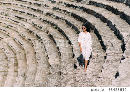 Girl walking on the steps of an ancient amphitheater, located in Hierapolis, Pamukkale, Denizli province, Turkey. Beautiful girl on the steps. Girl in white dress on stone stairs 83423652
