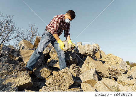 a man works with a pile of stones and broken pieces of concrete, carries construction debris 83426578