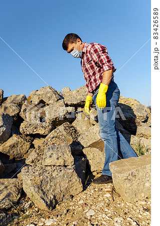 a man works with a pile of stones and broken pieces of concrete, carries construction debris 83426589