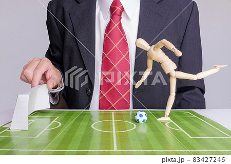 ゴールポストを動かすスーツを着た男性とシュートを打つデッサン人形 83427246