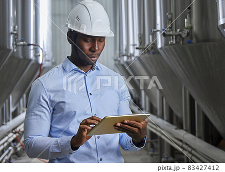 Portrait of a professional industrial engineer. Technician engineer in a safety helmet with a tablet. Large industrial plant background 83427412