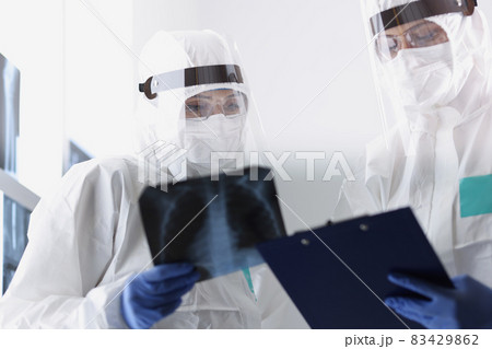Close-up of therapists in protective medical suits looking carefully at radiograph of sick patient Close-up of therapists in protective medical suits looking carefully at radiograph of sick patient 83429862