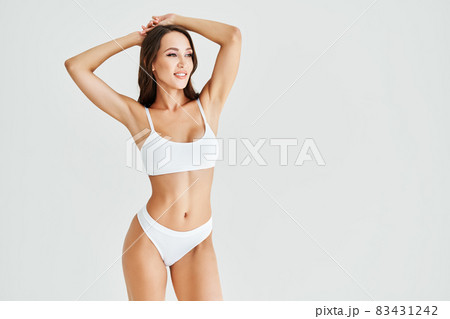 Smiling sporty woman in white underwear posing on studio background with copy space Smiling sporty woman in white underwear posing on studio background with copy space 83431242