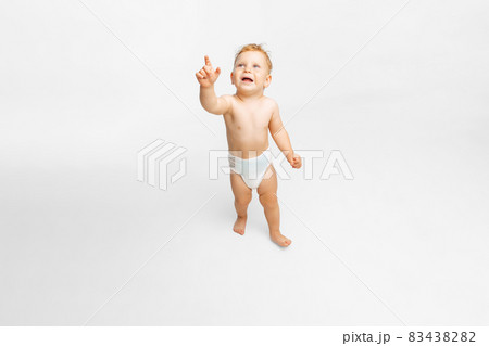 Full-length portrait of little boy, child in diaper in motion, walking pointing somewhere isolated over white background 83438282