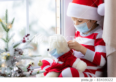 Happy child wearing Christmas pajamas sitting on windowsill Happy child wearing Christmas pajamas sitting on windowsill 83439322