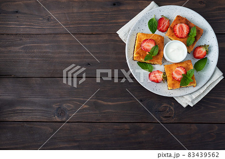 Cottage cheese casserole with strawberries and mint. Delicious homemade dessert made of curd and fresh berries with cream. dark wooden background, copy space. 83439562