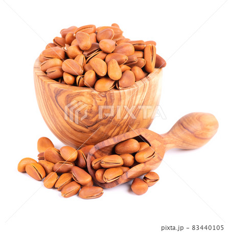 Pine nuts in olive bowl and scoop, isolated on white background. Heap of roasted pine nuts in shells. 83440105