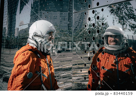 Portrait of smiling astronaut wearing orange spacesuit and space helmet near an abstract mirror wall. Portrait of smiling astronaut wearing orange spacesuit and space helmet near an abstract mirror wall. 83440159
