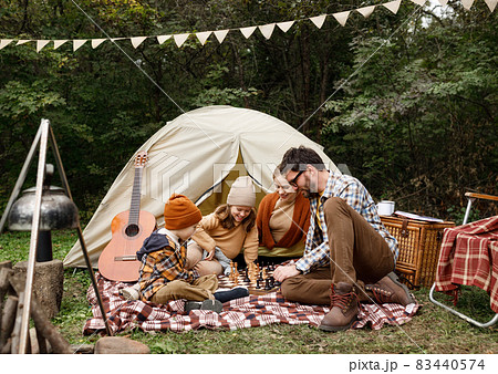 Happy smiling family playing chess game at campsite during camping trip in nature 83440574