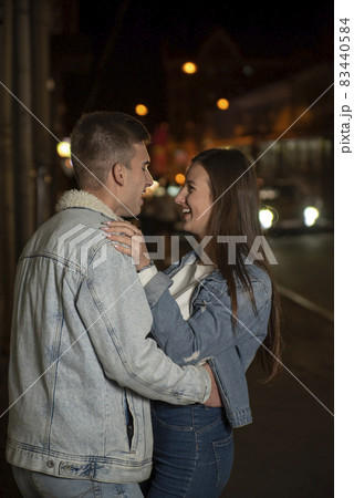 Laughing young people hug in the street. Evening date, young couple in love. Beautiful girl hugs a guy 83440584