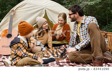 Happy smiling family playing chess game at campsite during camping trip in nature 83441090