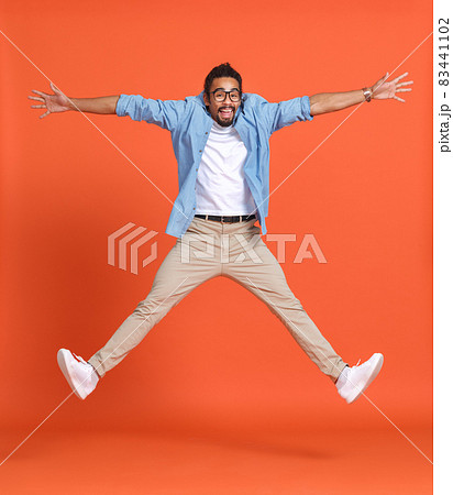 Full length shot of young emotional overjoyed african american man jumping over orange background Full length shot of young emotional overjoyed african american man jumping over orange background 83441102