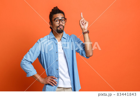 Young serious african american man in casual clothes pointing up at copy space with forefinger Young serious african american man in casual clothes pointing up at copy space with forefinger 83441843