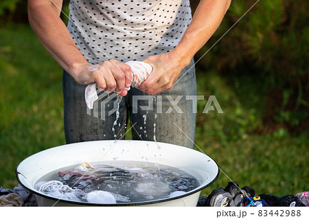 Woman wrings out underwear to an old basin outdoors in summer Woman wrings out underwear to an old basin outdoors in summer 83442988