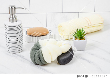 Herb soap, shower sponge and shampoo pump bottle inside a bright bathroom. 83445257