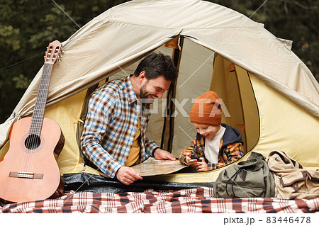 Father and little son reading map and using compass while sitting in touristic tent at campsite Father and little son reading map and using compass while sitting in touristic tent at campsite 83446478