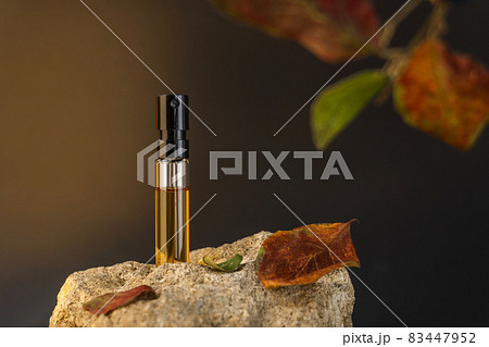 Beautiful glass sprayer bottle standing on a stone with apple leaves. Autumn cosmetic concept composition. Wooden scent perfume sample presentation. Luxury product advertising concept or mockup 83447952