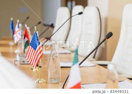 National flags placed on wooden conference table with microphones, papers and bottles of water 83449331