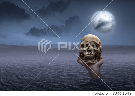 Hand raised from the sand and holding a human skull Hand raised from the sand and holding a human skull 83451948