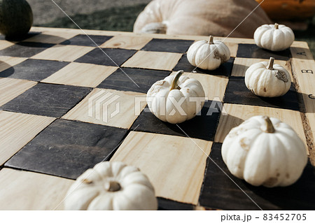 Small white Halloween pumpkins as garden decoration on a classic wood chess or checkers board. Halloween and Thanksgiving natural DIY ideas for home and celebration concept. Close up, copy space 83452705