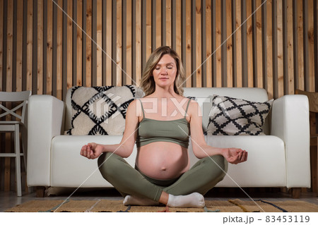 Pregnant woman meditates sitting on living room floor 83453119