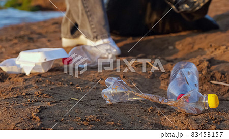 Unrecognizable woman in gloves collects plastic bottles in a black package near the river Unrecognizable woman in gloves collects plastic bottles in a black package near the river 83453157