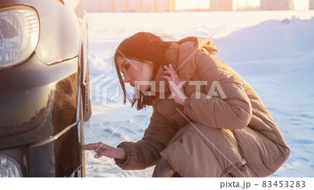 Lady checks wheel tire of broken automobile on snowy road Lady checks wheel tire of broken automobile on snowy road 83453283