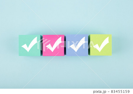 Four white checkmarks on multicolored cubes in a row against bright pastel blue background Four white checkmarks on multicolored cubes in a row against bright pastel blue background 83455159