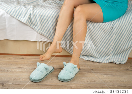 Cropped photo of adult female slender legs putting on cozy home slippers, sitting on the bed at home Cropped photo of adult female slender legs putting on cozy home slippers, sitting on the bed at home 83455252