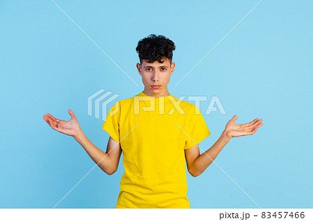 Cropped portrait of young boy in yellow T-shirt spreading hands isolated over blue background. Expression Cropped portrait of young boy in yellow T-shirt spreading hands isolated over blue background. Expression 83457466