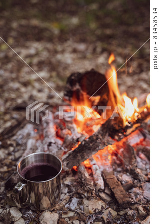 A metal mug with a drink stands next to the fire. Picnic in a camp in the woods. Fireplace in the camp, twilight 83458534