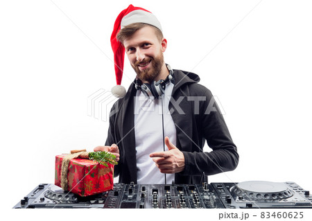 Funny dj guy in Santa's hat holds gift box while standing behind a turntable. New Year party Funny dj guy in Santa's hat holds gift box while standing behind a turntable. New Year party 83460625