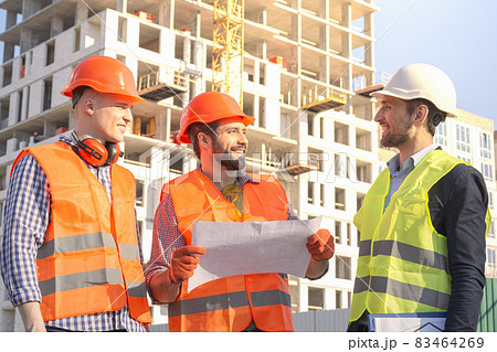 Male workers engineers at construction site in helmets hardhats near high-rise building skyscraper. Two construction engineers inspect the construction site. Male workers engineers at construction site in helmets hardhats near high-rise building skyscraper. Two construction engineers inspect the construction site. 83464269