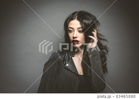 Fashion woman with beautiful face in a leather jacket with beautiful long dark hair isolated on gray background. Young female model with professional make-up. Cosmetics Fashion woman with beautiful face in a leather jacket with beautiful long dark hair isolated on gray background. Young female model with professional make-up. Cosmetics 83465880