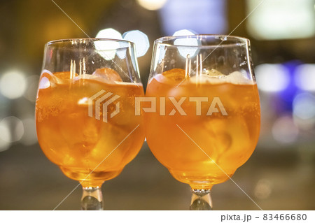Two glasses of wine with orange coctail stand on a wooden table in a cafe.Italian alcoholic drink with oranges and ice. Close-up, selective focus Two glasses of wine with orange coctail stand on a wooden table in a cafe.Italian alcoholic drink with oranges and ice. Close-up, selective focus 83466680