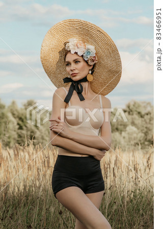 Girls in tops and shorts, in a hat and with a rim of flowers, posing against the background of nature. The first girl holds the stems of the reed. Another girl with a basket in which different flowers Girls in tops and shorts, in a hat and with a rim of flowers, posing against the background of nature. The first girl holds the stems of the reed. Another girl with a basket in which different flowers 83466951